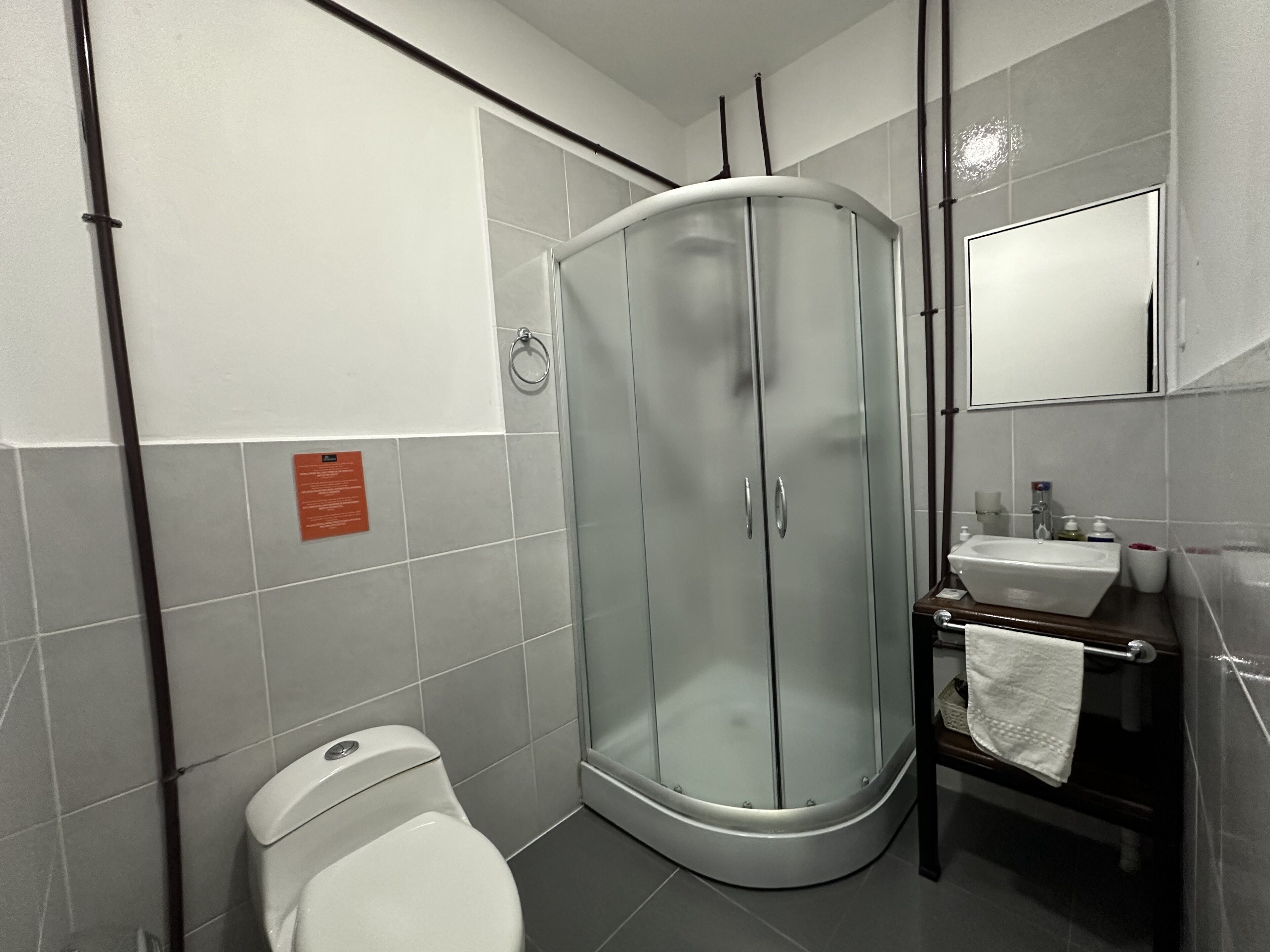 Un baño moderno con cabina de ducha de vidrio, inodoro y lavamanos con espejo superior.