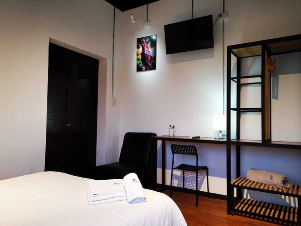 Un dormitorio con cama, escritorio, silla y televisor en la pared.