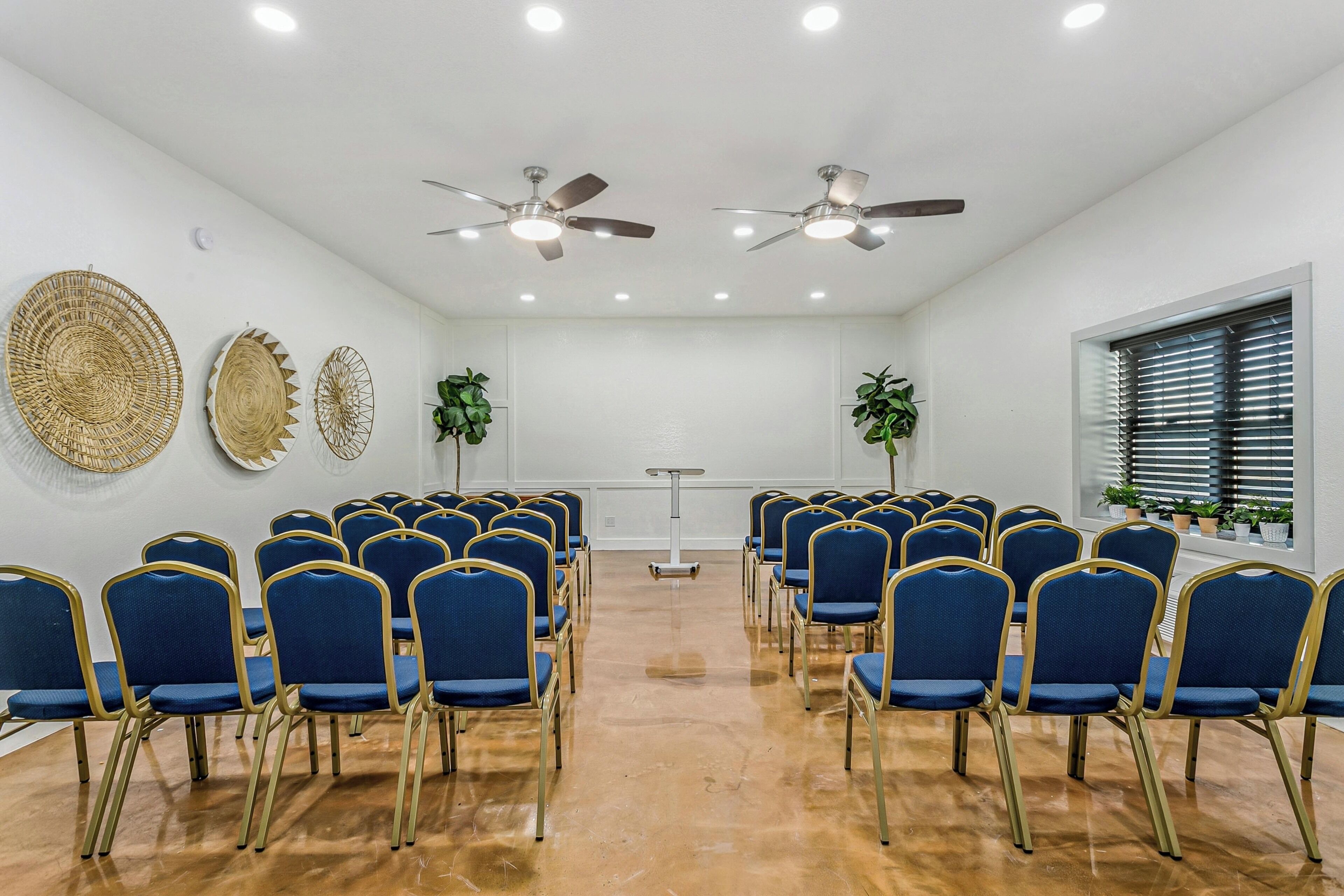 A conference room with rows of blue chairs, ceiling fans, and decorative wall art.