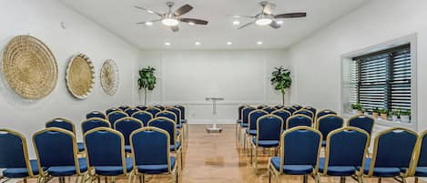 A conference room with rows of blue chairs, ceiling fans, and decorative wall art.
