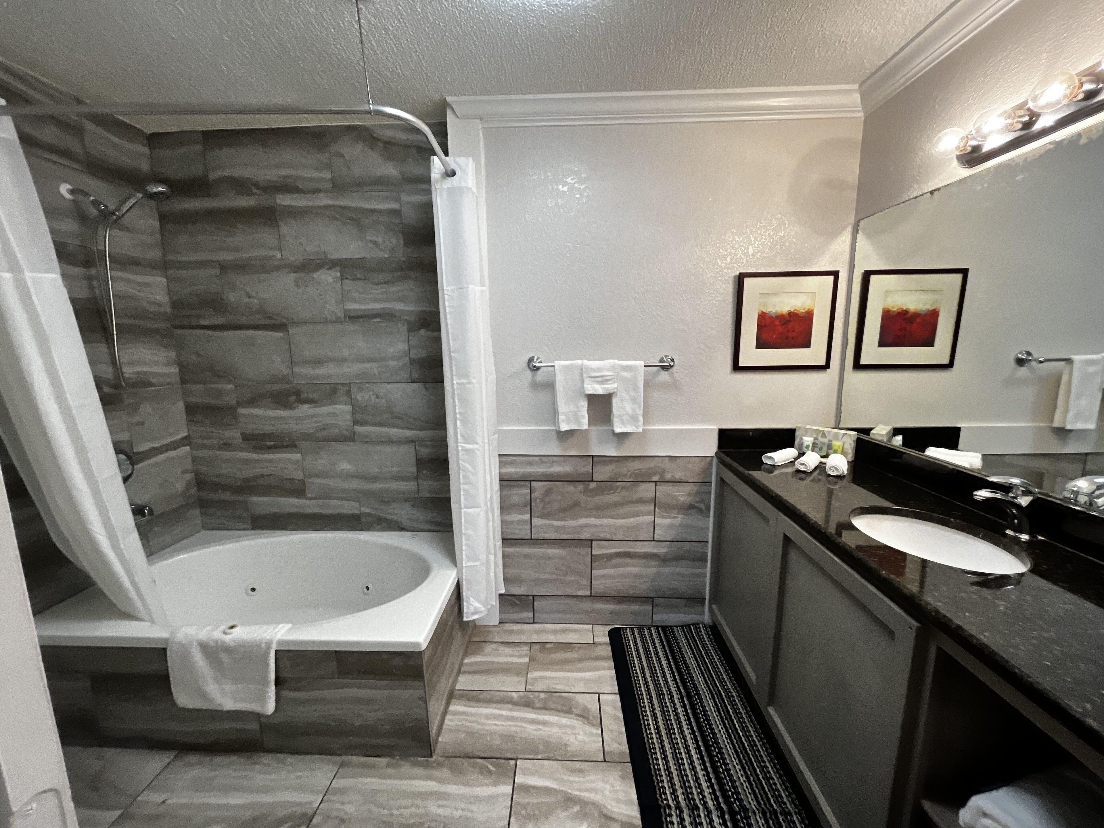 A modern bathroom with a stone shower enclosure, a bathtub, a vanity with a sink, and a large mirror.