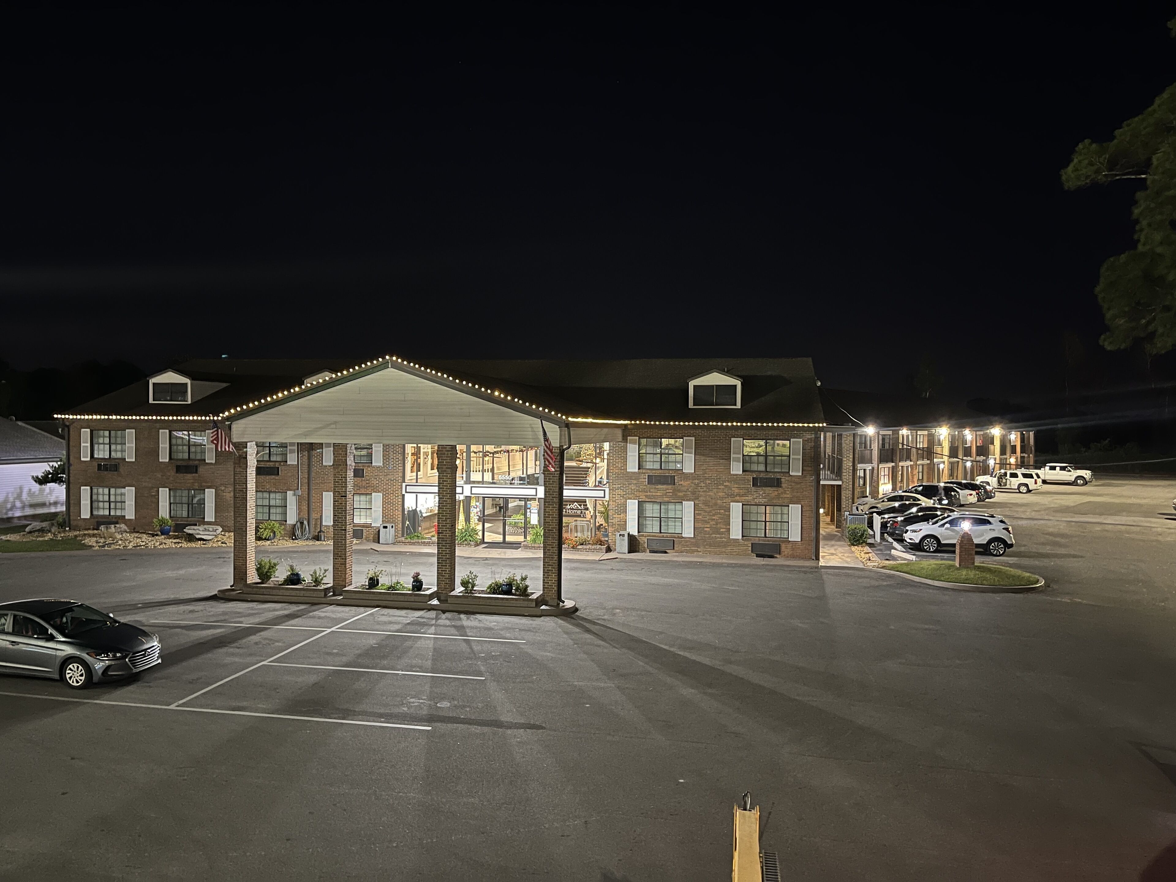 Un motel doté d’un parking couvert, où plusieurs voitures sont stationnées, et dont l’entrée est bien éclairée.