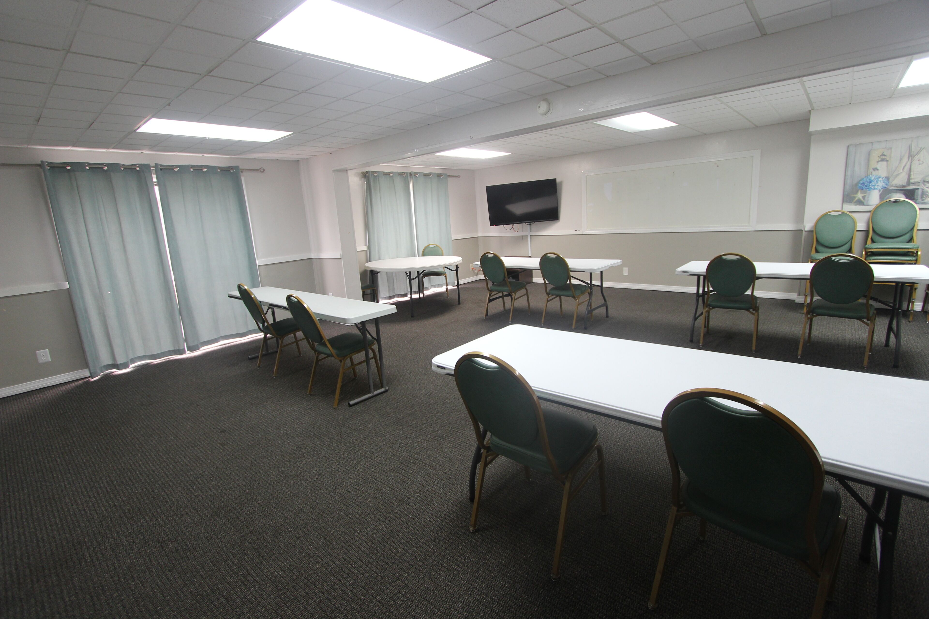 Un salón de conferencias con una larga mesa, varias sillas, un televisor de pantalla plana y una pizarra.