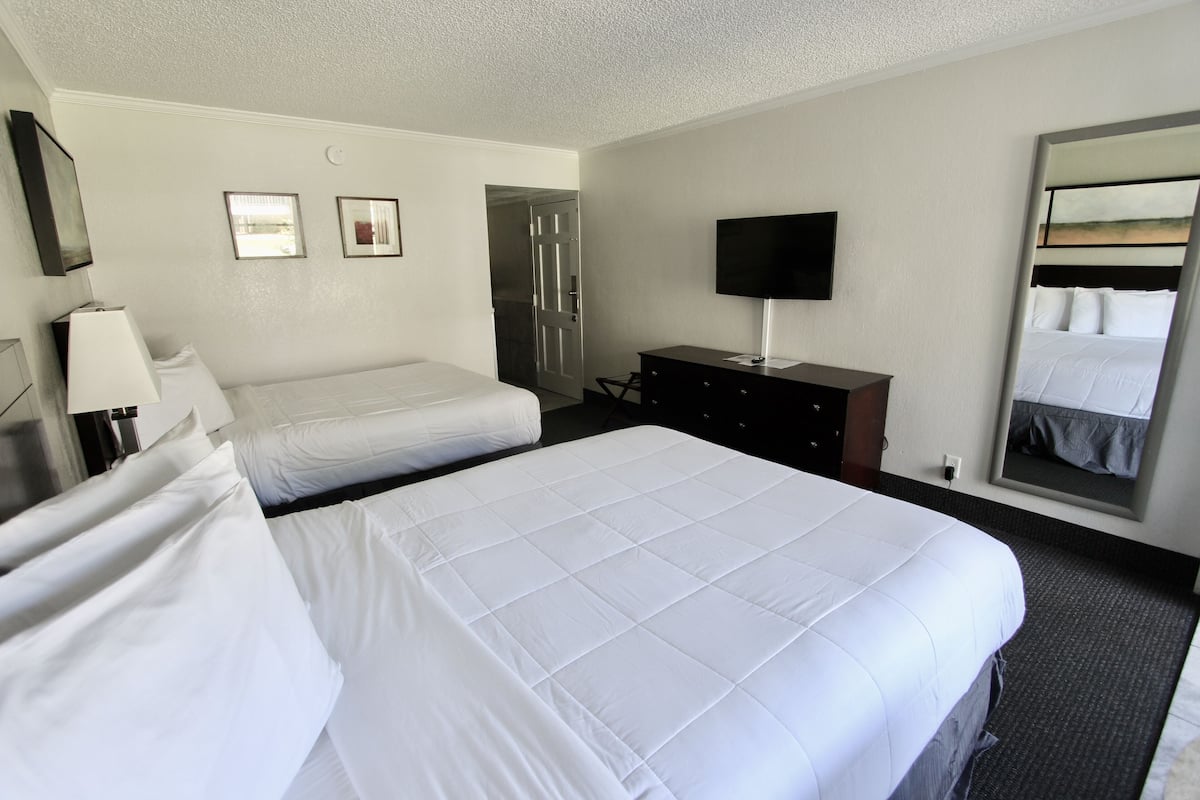 A hotel room with two beds, a TV, a dresser, and a mirror.
