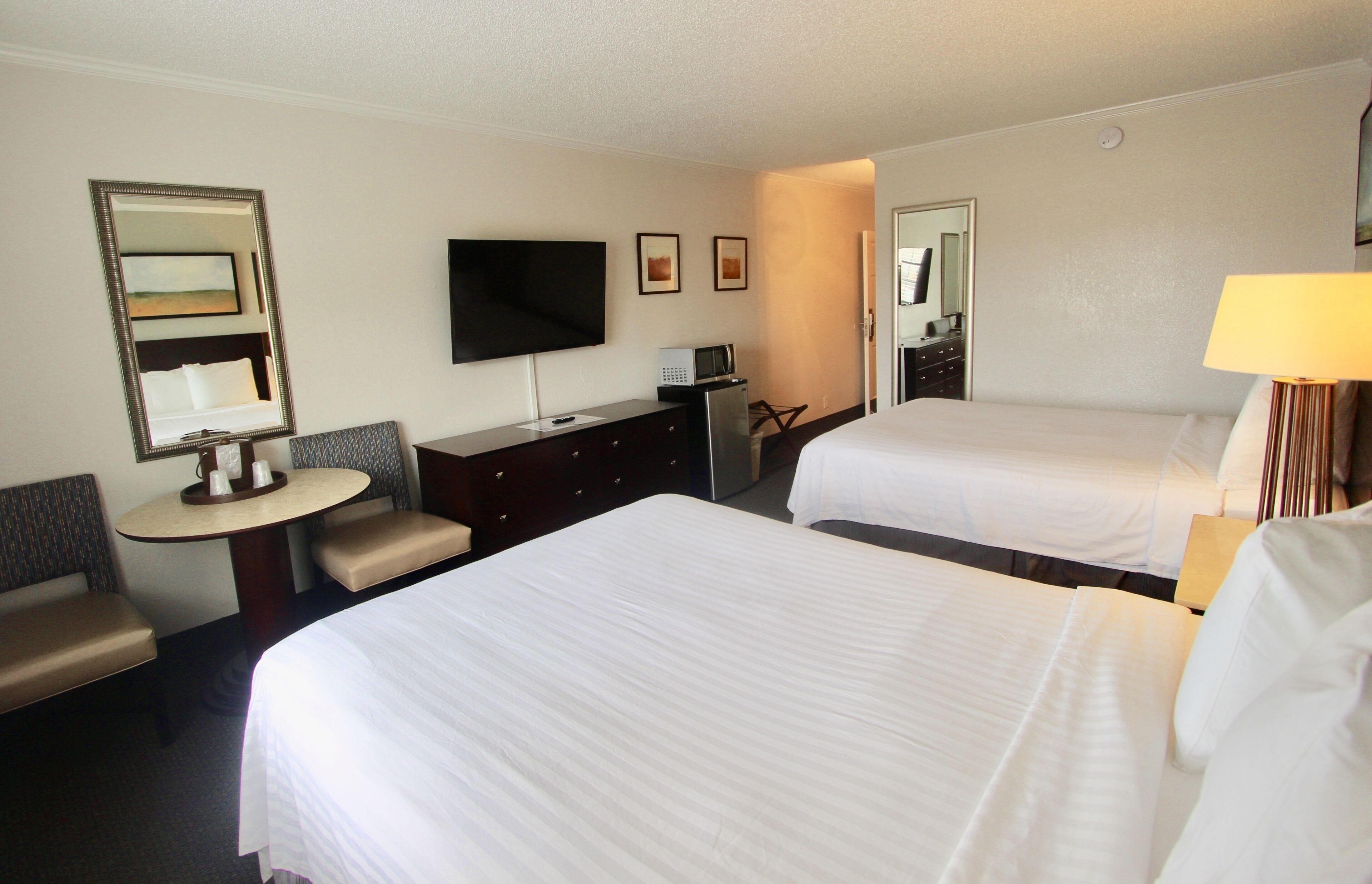 A hotel room with two beds, a desk, a chair, a television, and a mirror.