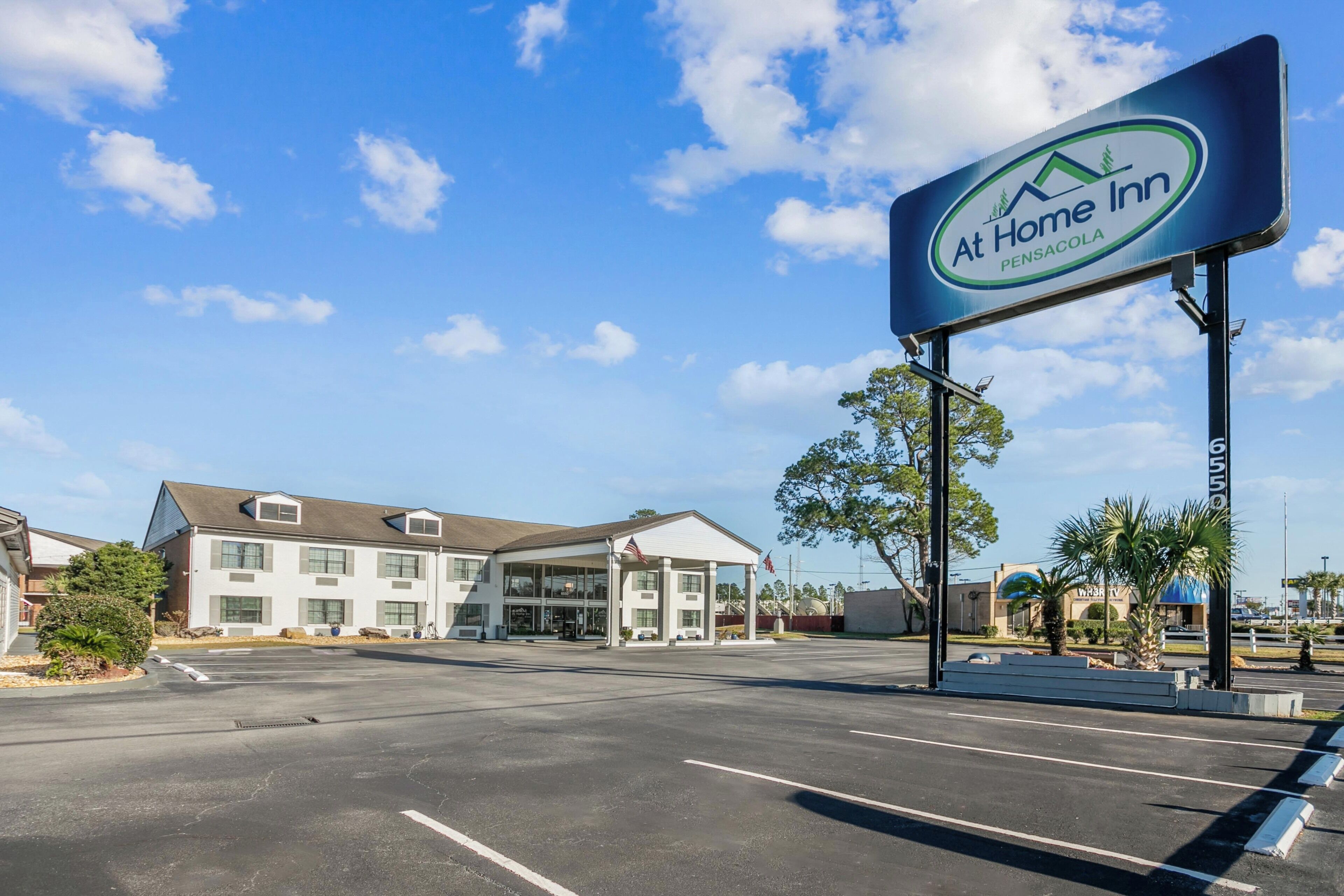 Un hotel con cielo despejado, estacionamiento y un letrero que dice 'At Home Inn Pensacola'.