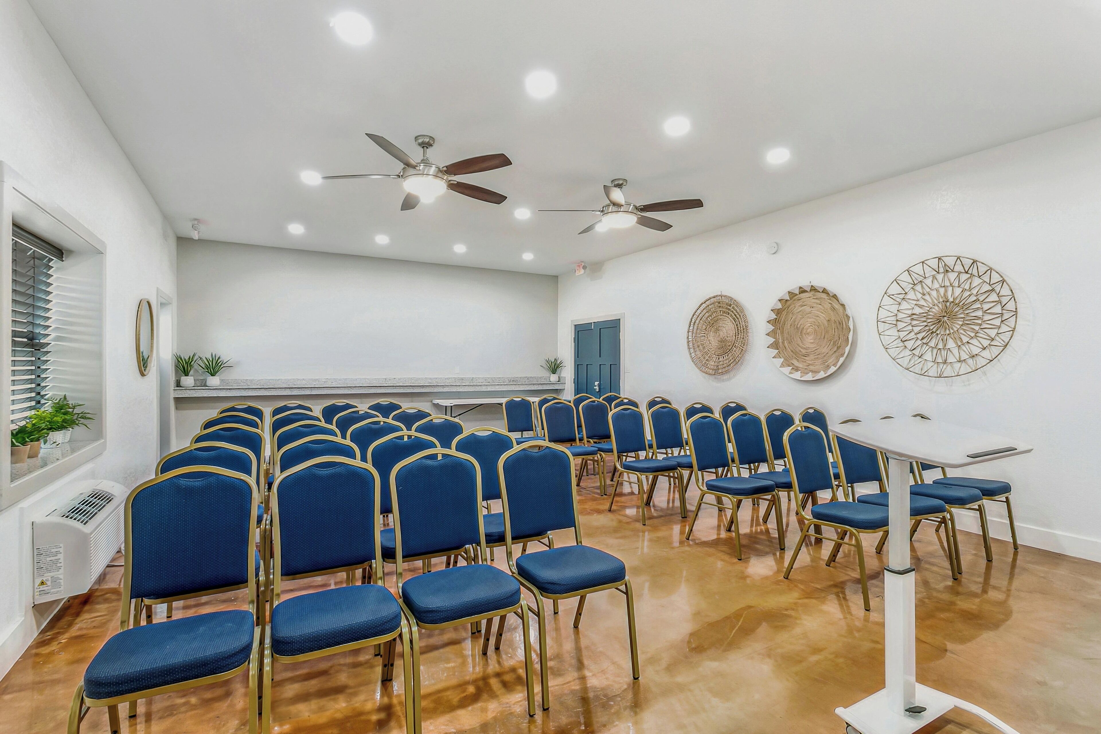 A conference room with rows of blue chairs, ceiling fans, and decorative wall art.