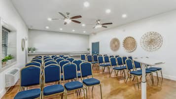 A conference room with rows of blue chairs, ceiling fans, and decorative wall art.