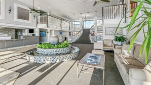 Un salón amplio con una distribución central de asientos, una escalera que conduce a un nivel superior y vistas al exterior.