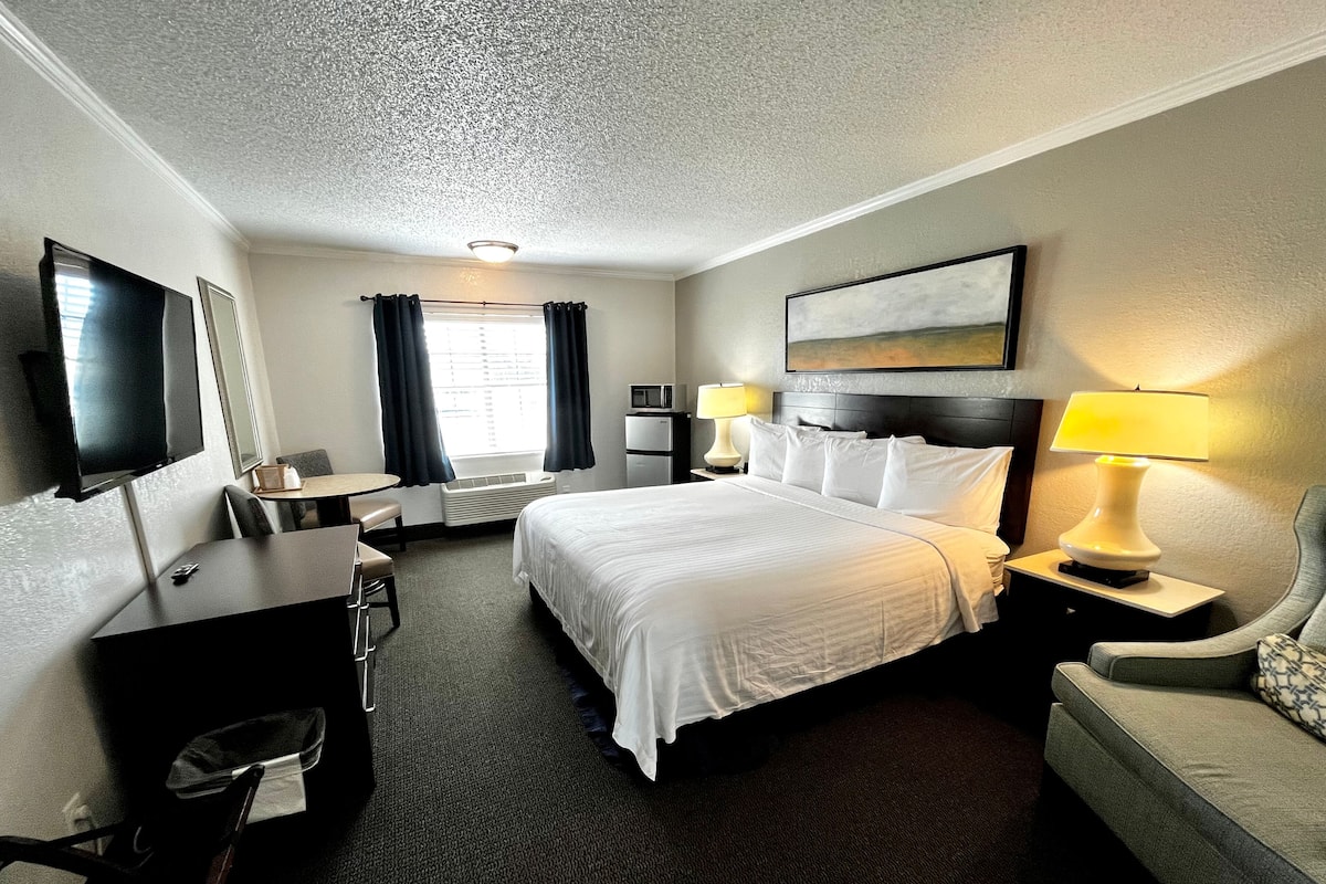 A hotel room with a bed, bedside tables, a desk, a chair, a TV, and a window with curtains.