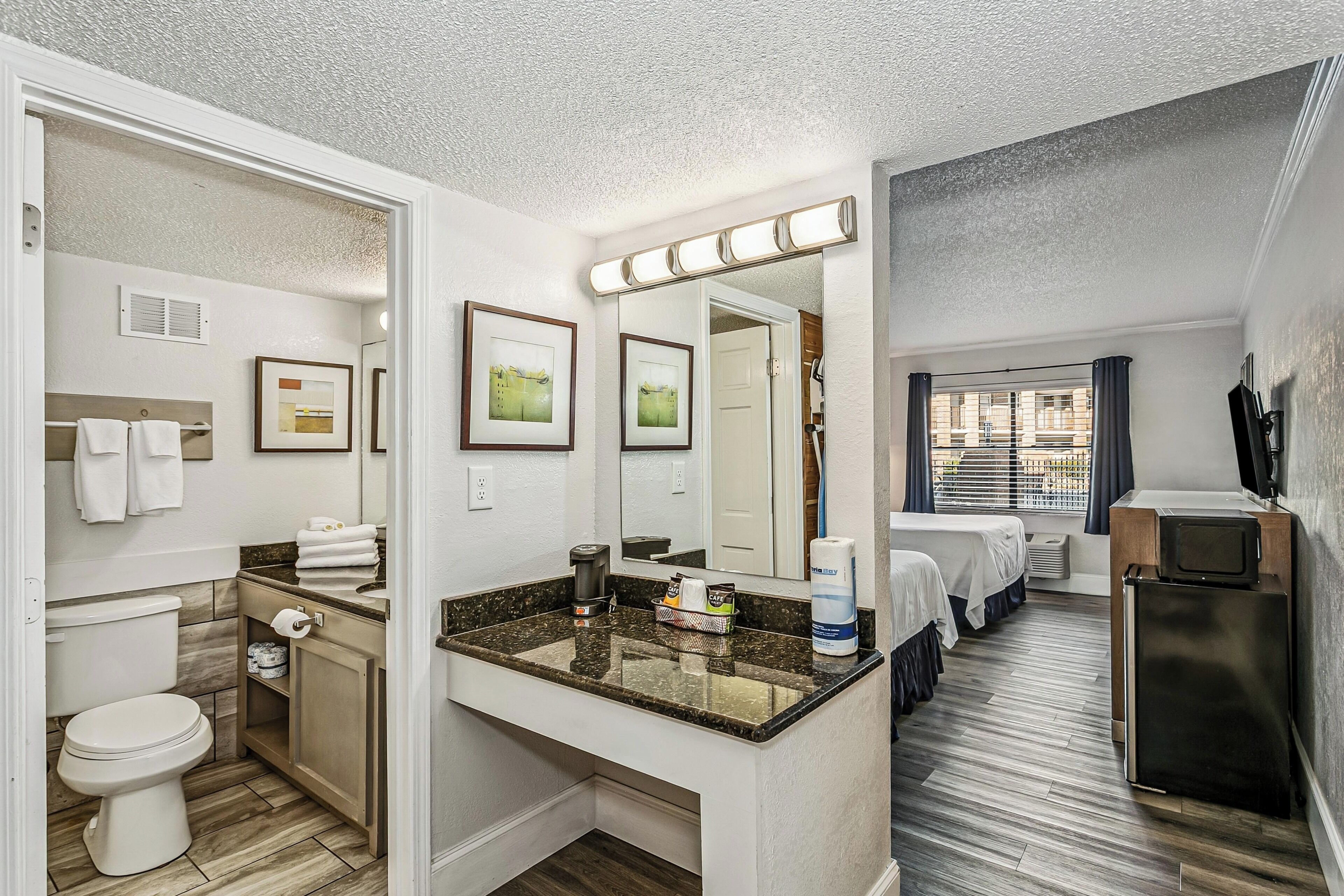 A hotel bathroom with a toilet, sink, mirror, and towel rack.