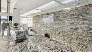 Un moderno vestíbulo de hotel con un mostrador de recepción de mármol, una pared con diseño de ladrillos y un cartel que dice 'At Home Inn & Suites'.