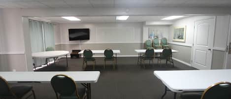A conference room with white tables and green chairs, a flat-screen TV, and a whiteboard.
