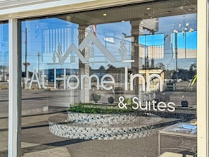 Une enseigne d’hôtel portant le nom « At Home Inn & Suites », avec le reflet de bâtiments et d’un ciel dégagé.