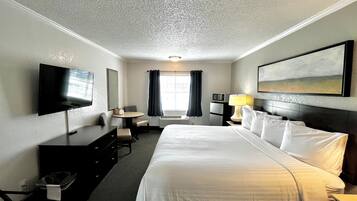 Habitación de hotel con cama, escritorio, silla, televisor, lámpara y un cuadro en la pared.