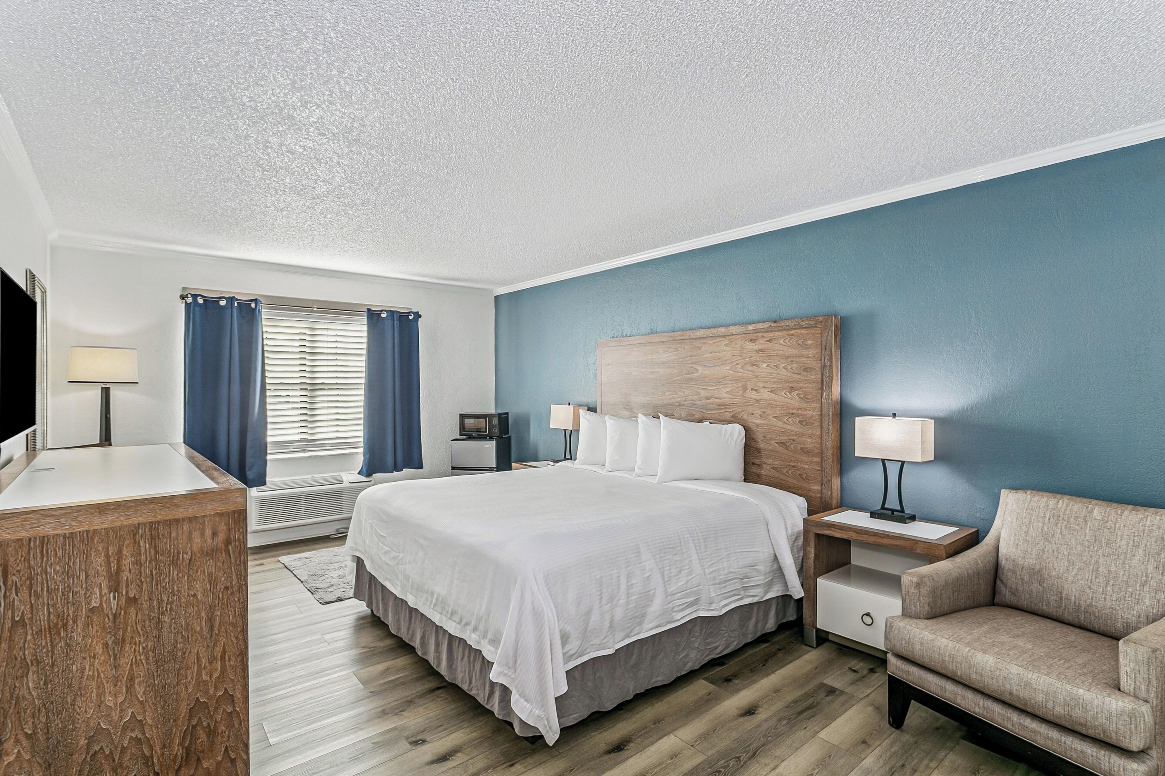 Une chambre d’hôtel comprenant un lit, des tables de chevet, une chaise, un bureau, une télévision et une fenêtre avec des rideaux.