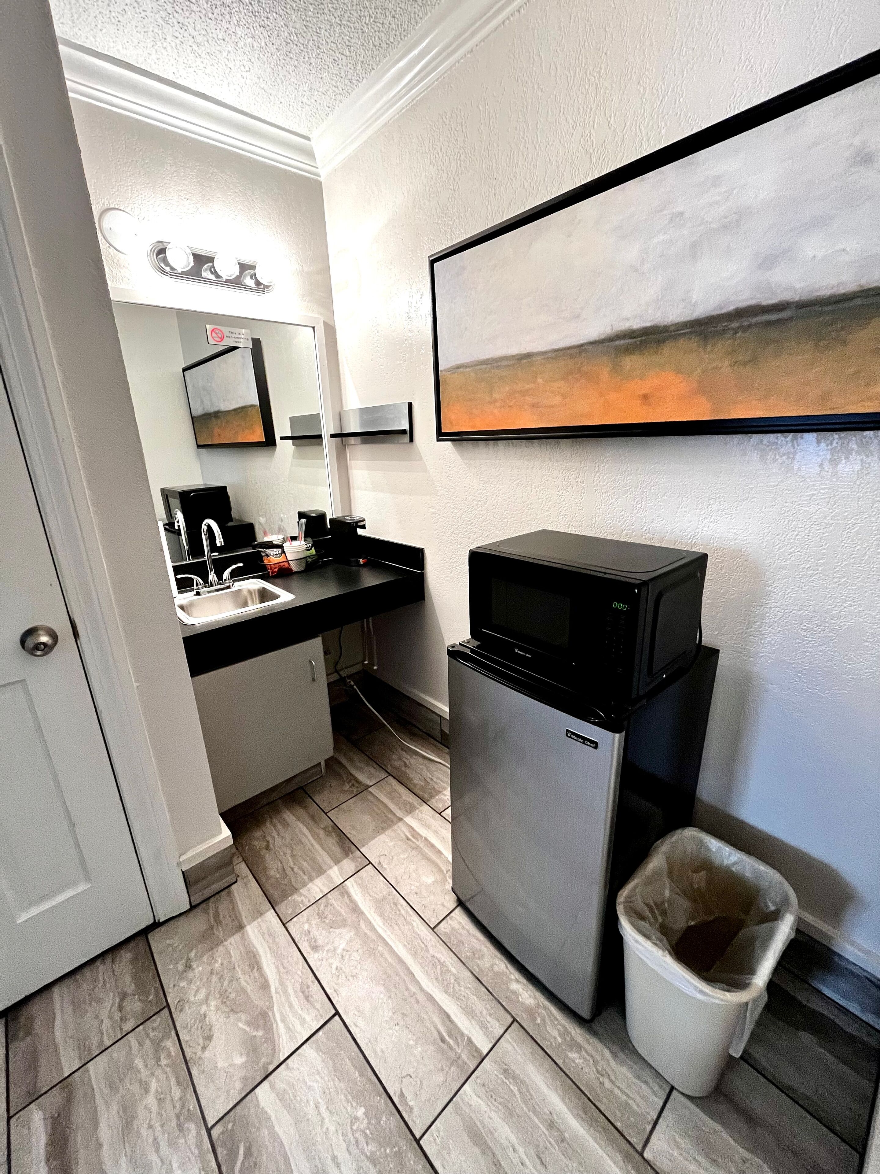 Un baño de hotel pequeño con lavamanos, espejo y refrigerador.