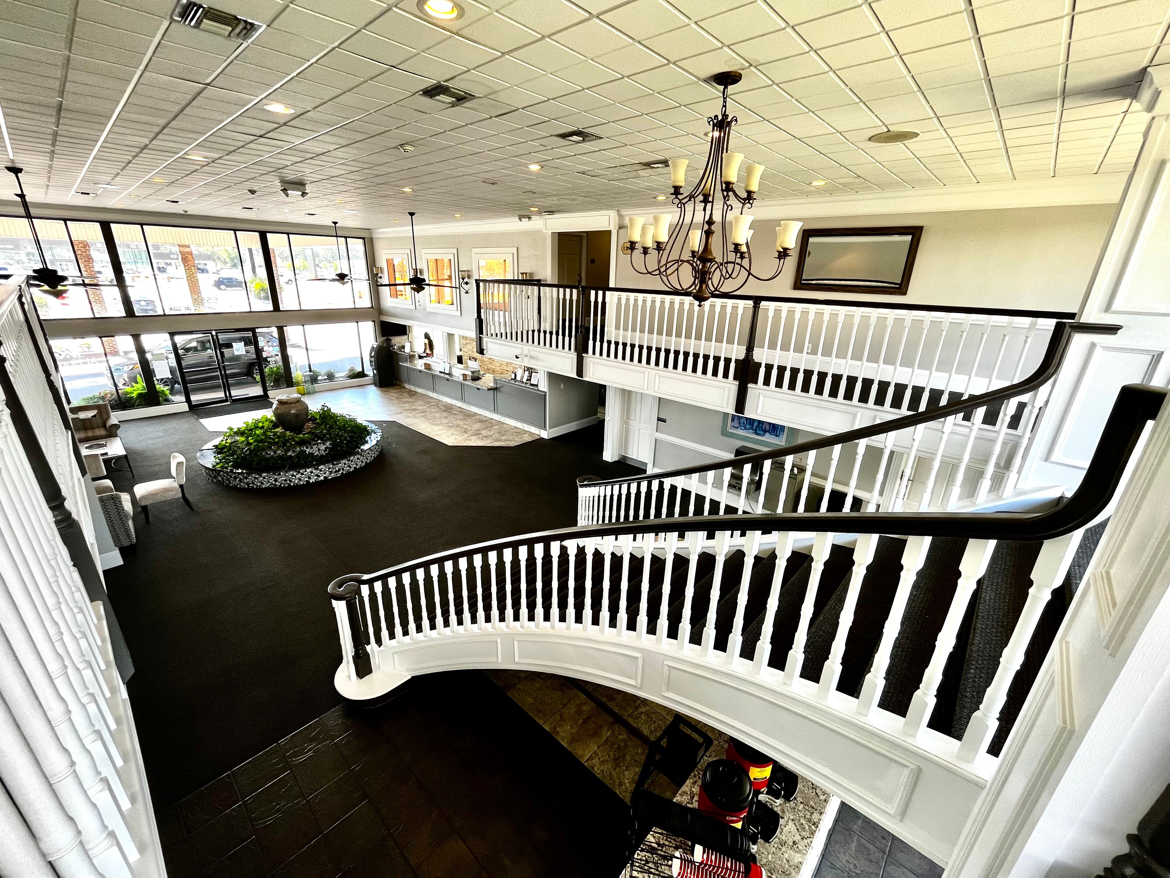 A spacious hotel lobby with a central seating area, a staircase with white balustrades, and a chandelier.