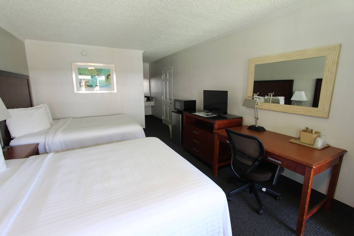 A hotel room with two beds, a desk with a computer, a chair, a desk lamp, and a large mirror.