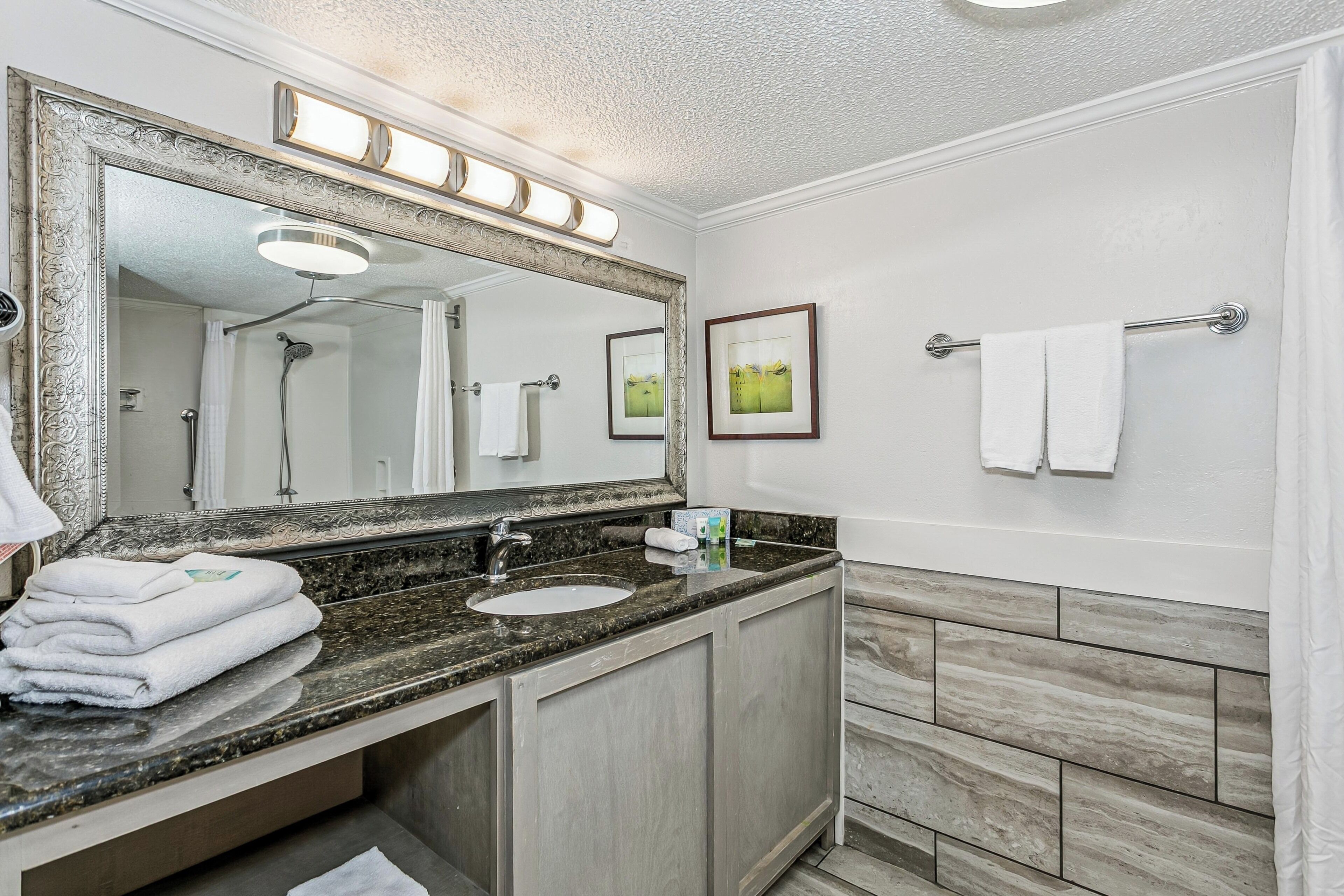 A bathroom with a large mirror, a sink, a towel rack, and a shower.