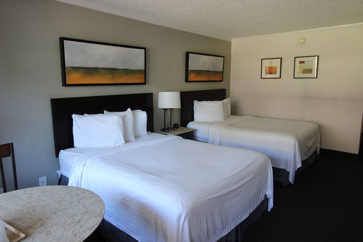 A hotel room with two beds, a round table, and artwork on the walls.
