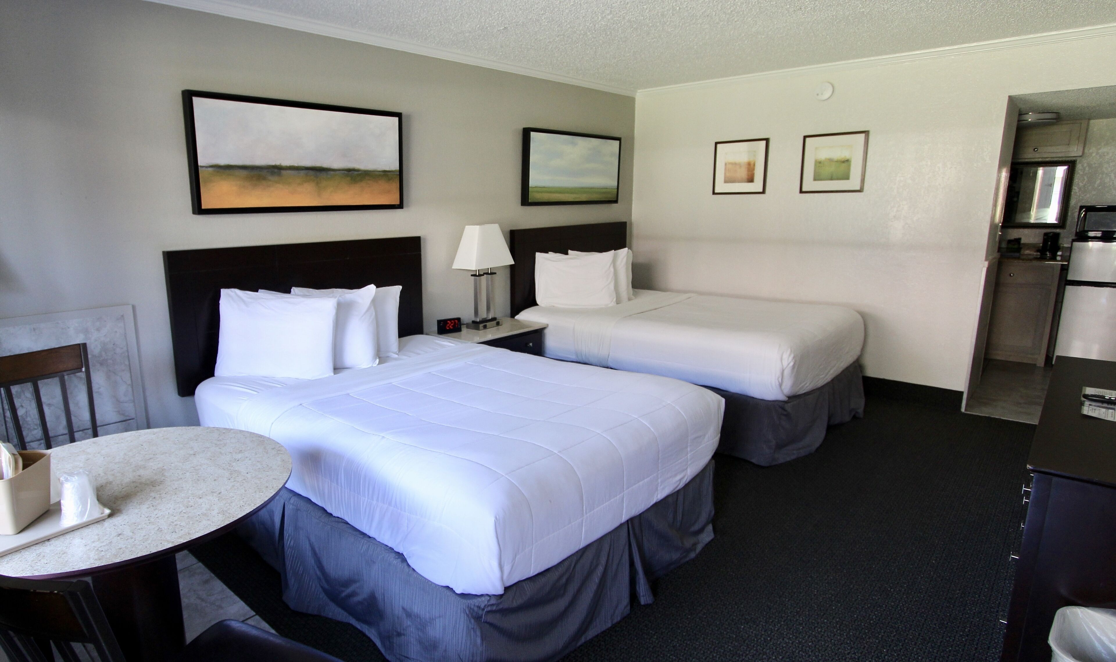 Een hotelkamer met twee bedden, een tafeltje, een stoel en een kitchenette.