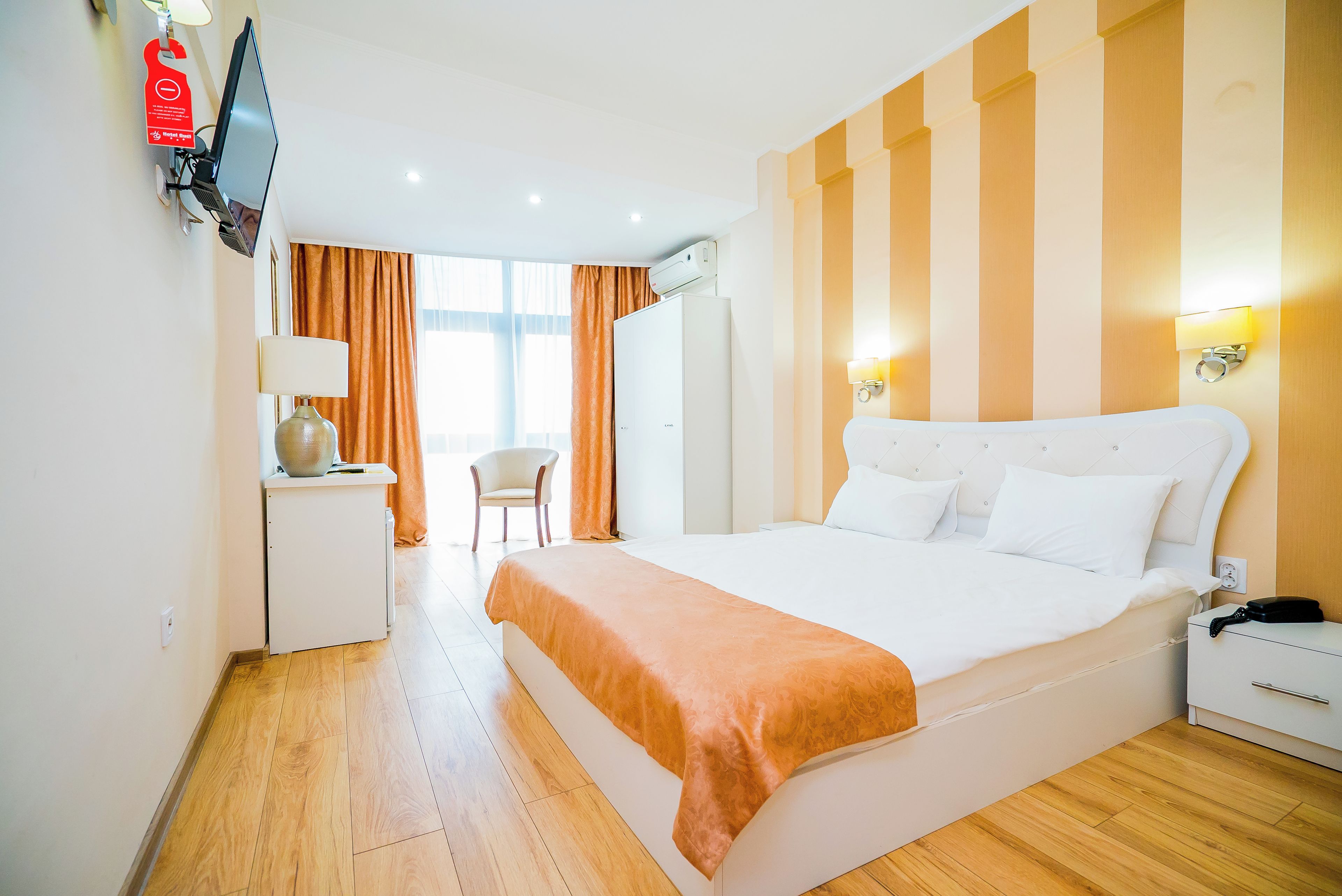 Ein Hotelzimmer mit einem großen Bett, einem Schreibtisch mit Lampe, einem Sessel und einem an der Wand befestigten Fernseher.