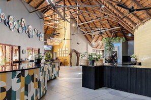 A spacious lobby with a high ceiling, a reception desk, and a variety of plants.