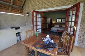 A cozy room with a wooden dining table, chairs, and a sofa. A kitchen area is visible with a gas cylinder and a bottle.