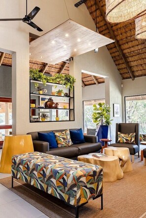 A modern living room with a high ceiling, wooden beams, and a large window. - Hippo Hollow Country Estate (Mbombela)