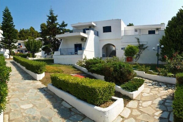 A modern building with a white facade, multiple balconies, and a stone pathway. - Muses (Skiathos)