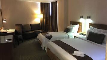 Habitación de hotel con dos camas, un escritorio, una silla, una lámpara y una ventana con cortinas.
