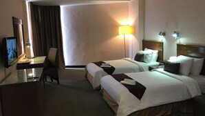 A hotel room with two beds, a desk with a television, a lamp, and a view of the outside.