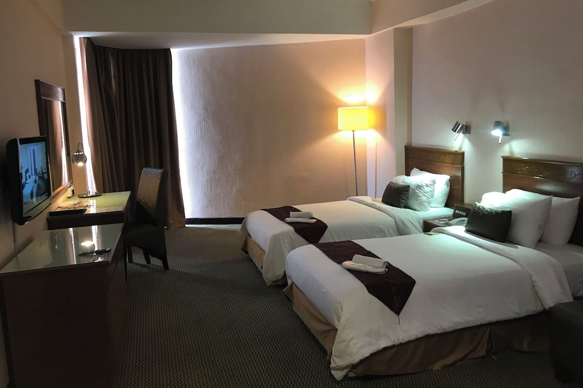 Habitación de hotel con dos camas, un escritorio con televisor, una lámpara y vista al exterior.