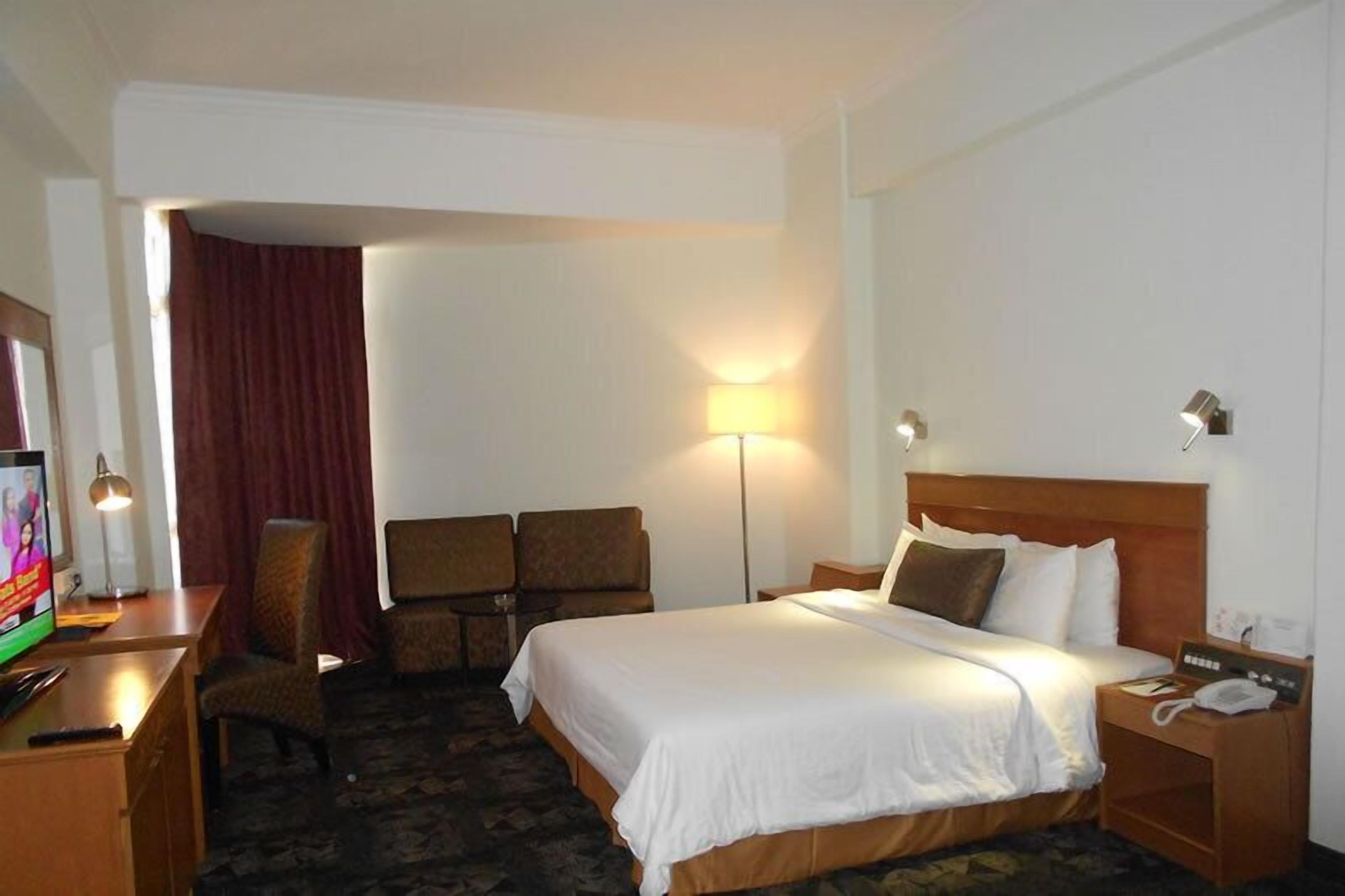 Habitación de hotel con cama, escritorio, silla, televisor y lámpara.