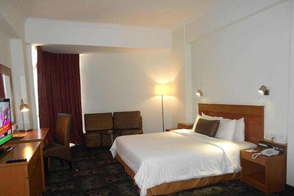 Une chambre d’hôtel comprenant un lit, un bureau avec une télévision, une chaise, une lampe et une table de chevet avec un téléphone.