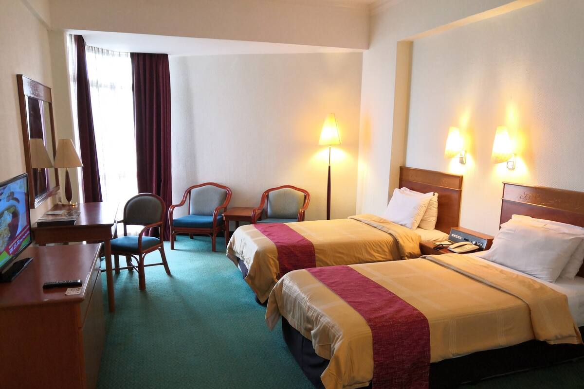 Une chambre d’hôtel avec deux lits, un bureau avec un ordinateur, une chaise et deux lampes.