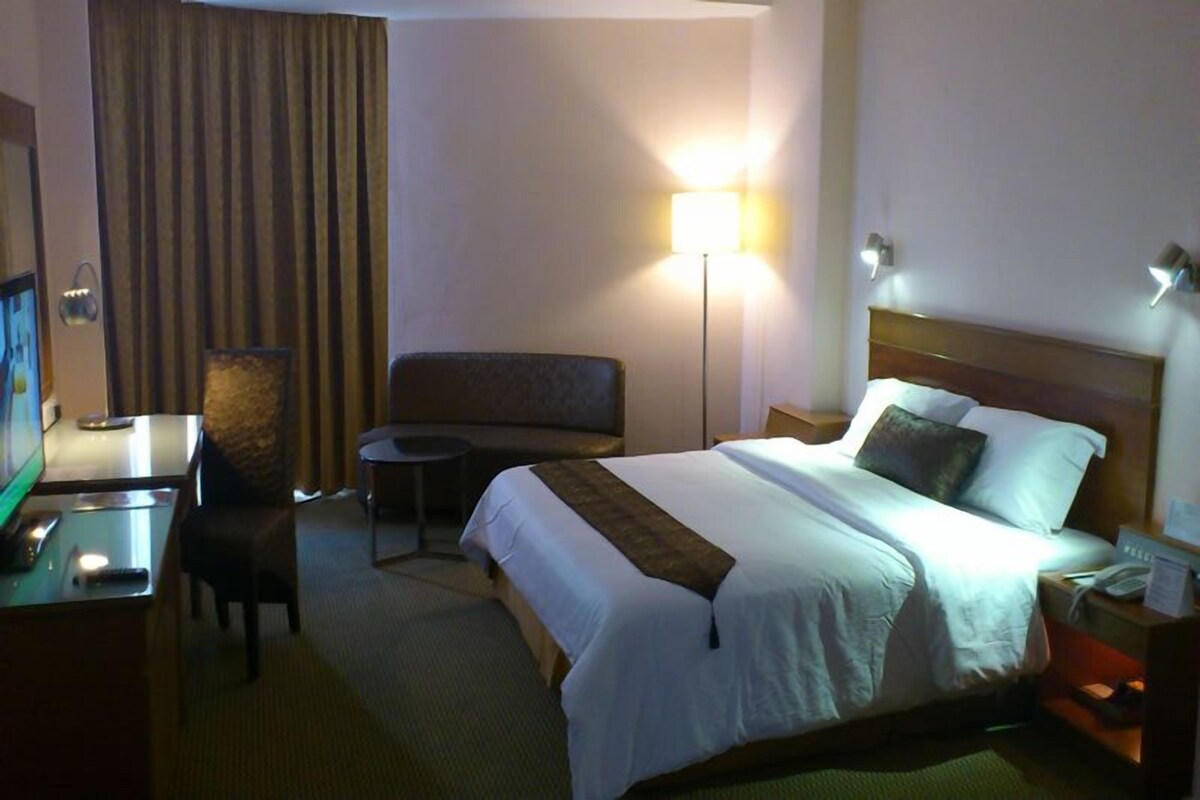 Una habitación de hotel con una cama, un escritorio con ordenador, una silla, un sofá y una lámpara.
