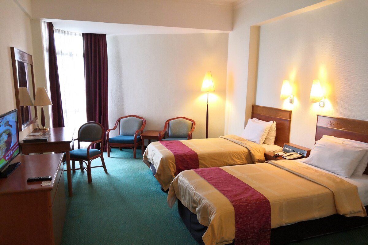 Habitación de hotel con dos camas, un escritorio con computadora, una silla y dos lámparas.