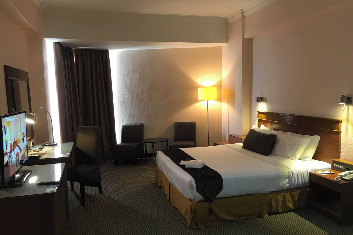 Une chambre d’hôtel comprenant un lit, un bureau avec un ordinateur, deux chaises, une lampe et un téléviseur.