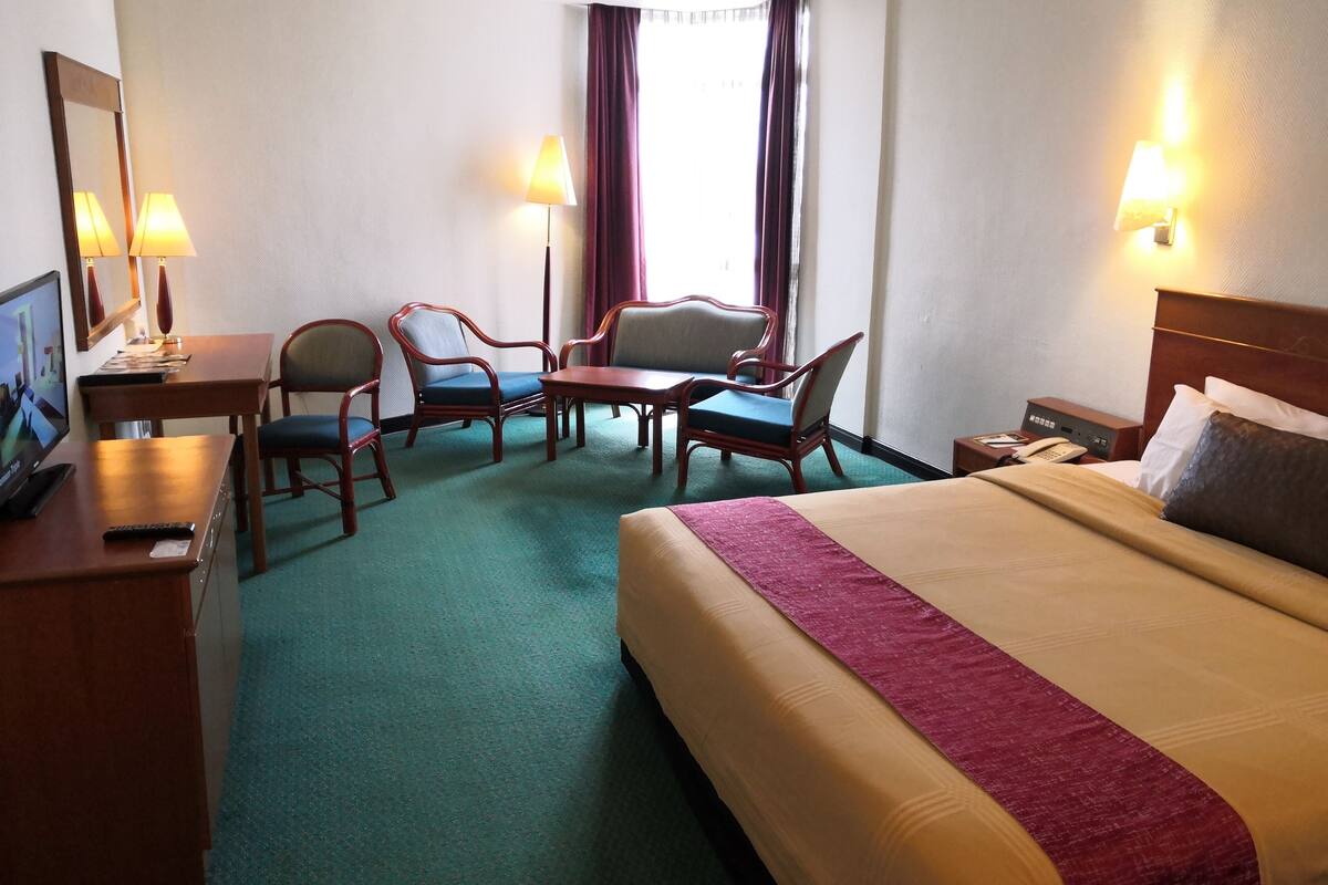 Une chambre d’hôtel comprenant un lit, deux fauteuils, une petite table, un bureau avec un ordinateur et un téléviseur.
