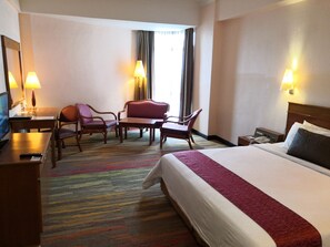 A hotel room with a bed, a desk with a computer, two chairs, a small table, and a window with curtains. - Hotel Grand Continental Kuala Terengganu (Kuala Terengganu)