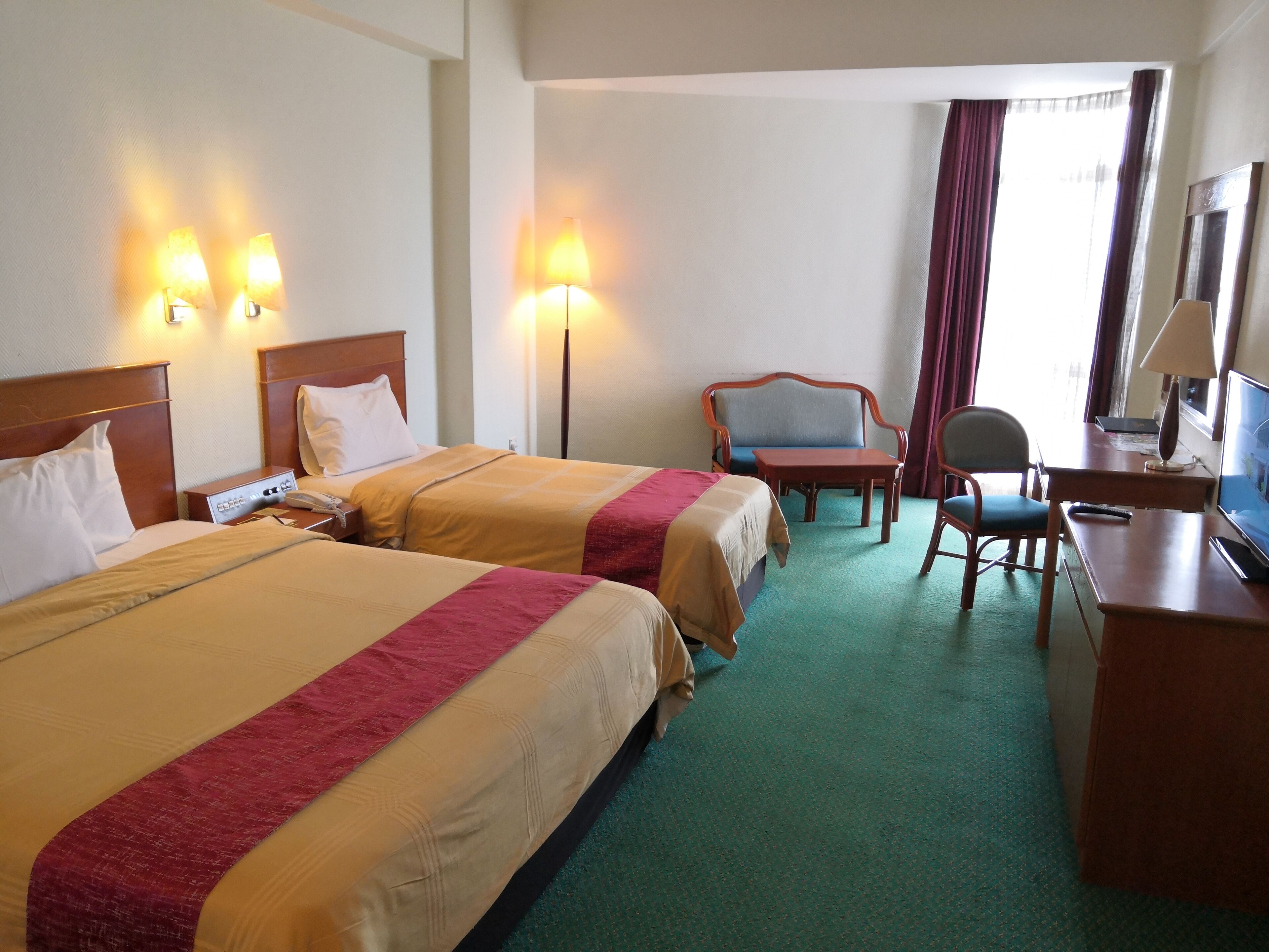 Habitación de hotel con dos camas, un escritorio, una silla, un televisor y una lámpara.