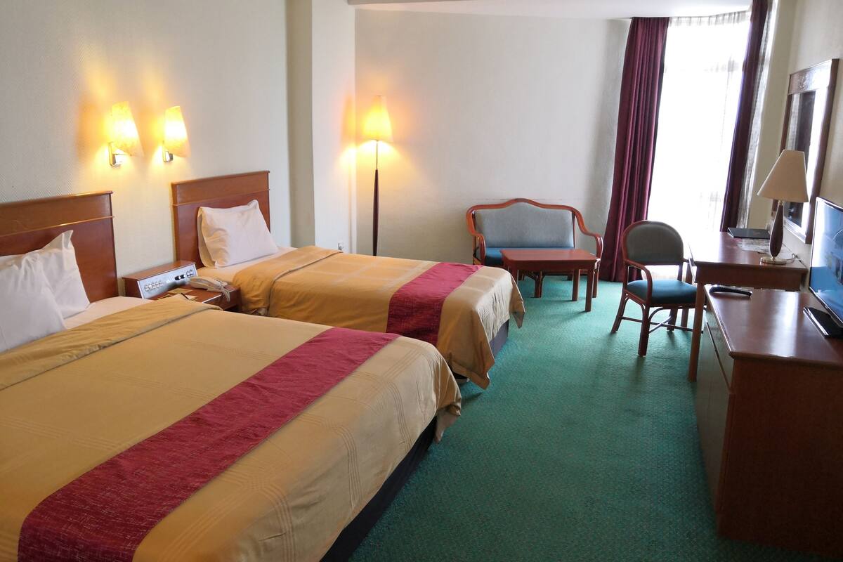 Une chambre d’hôtel avec deux lits, un bureau, une chaise, une télévision et une lampe.