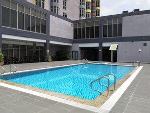 Una piscina con borde de baldosas, rodeada por un edificio con ventanales grandes y techo plano.