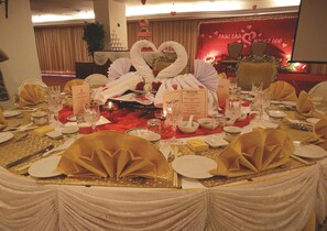 A formal dining setup with white and gold table settings, a heart-shaped centerpiece, and a red backdrop with the names "Paul Lau" and "Nick Lee".