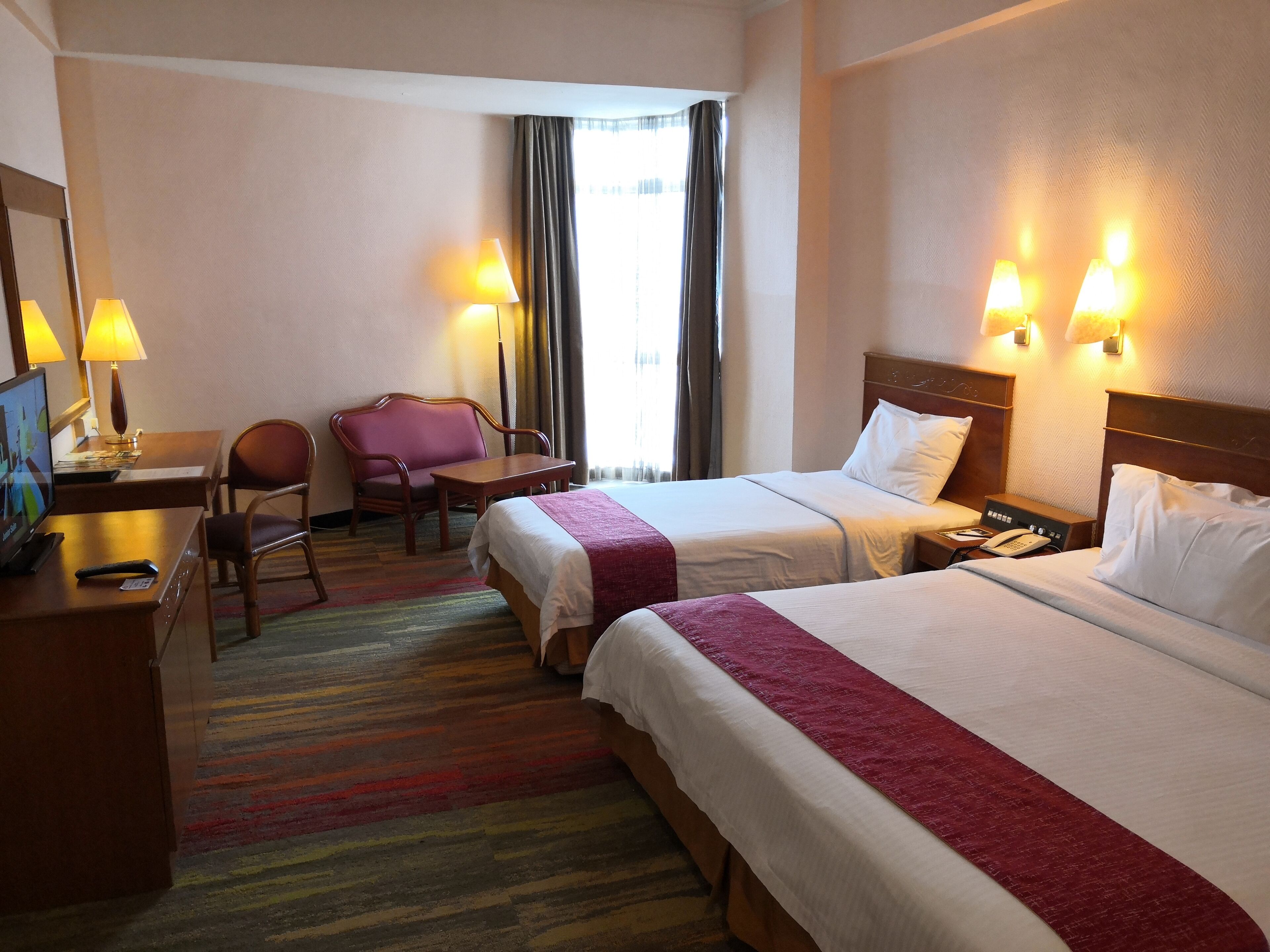 Habitación de hotel con dos camas, un escritorio con silla, un televisor y dos lámparas.