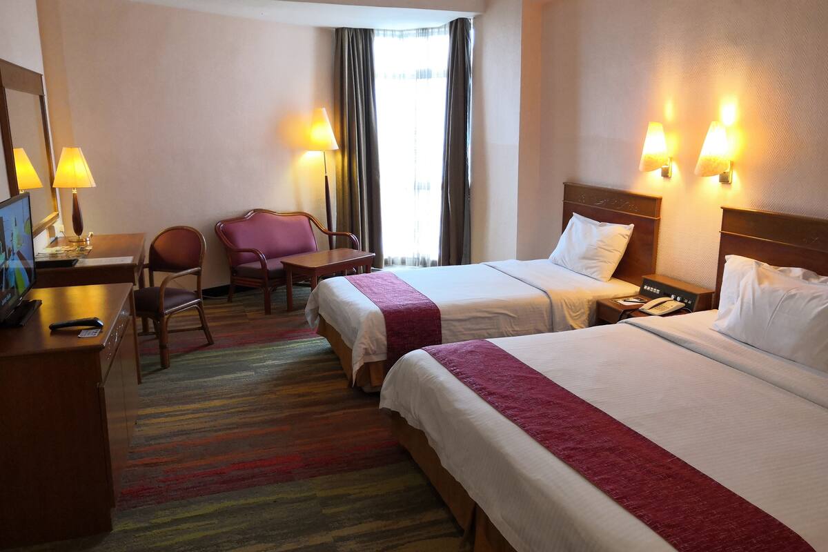 Une chambre d’hôtel avec deux lits, un bureau avec une chaise, une télévision et des lampes.