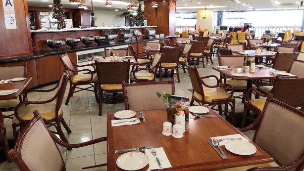 A spacious restaurant with wooden tables and chairs, a central bar area, and a view of the street outside.