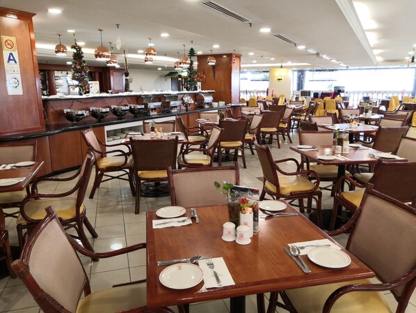 A spacious restaurant with wooden tables and chairs, a central bar area, and a view of the street outside.